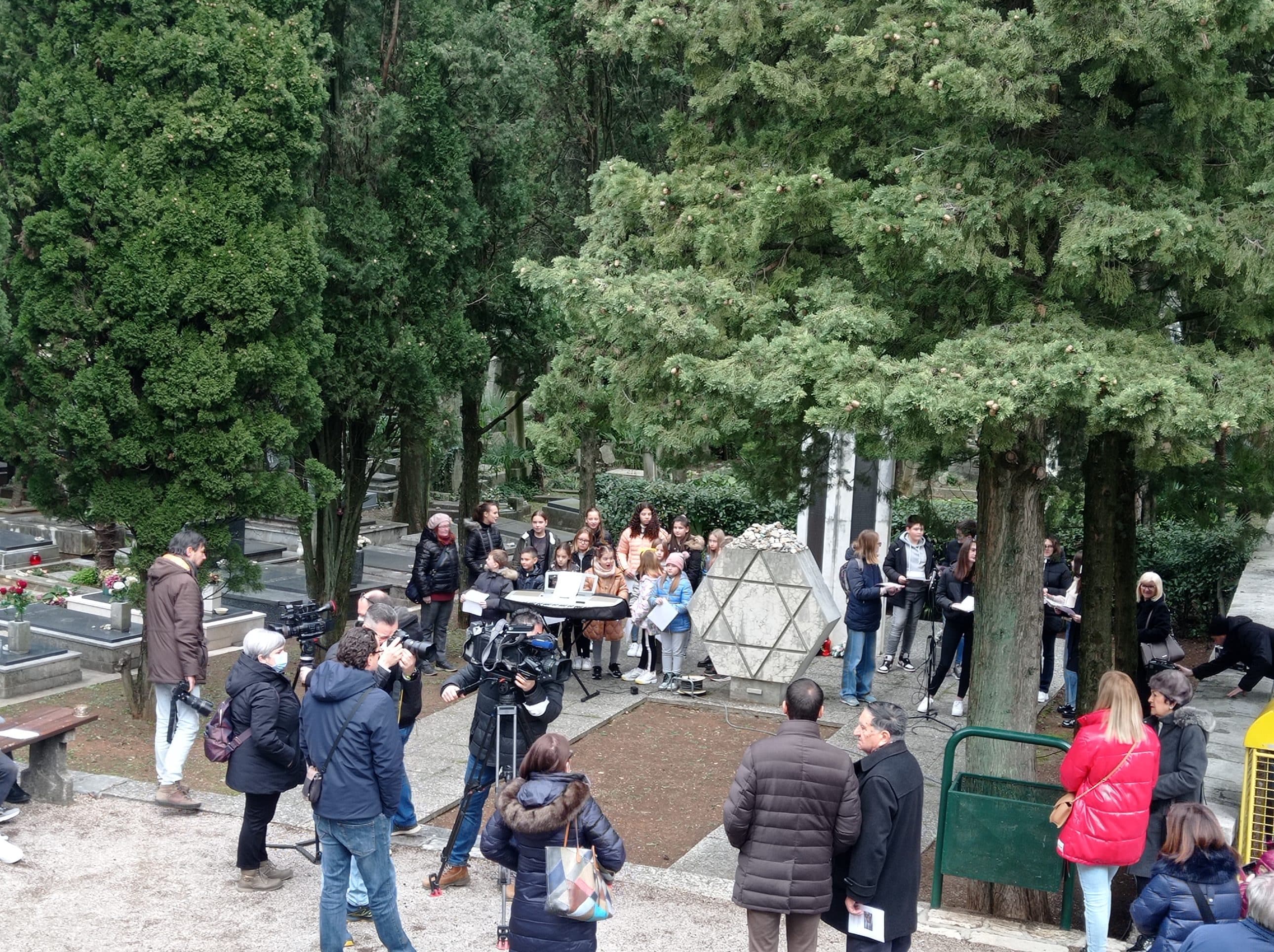 Okupljeni građani, novinari i zbor ispred spomenika s Davidovom zvijezdom na groblju.