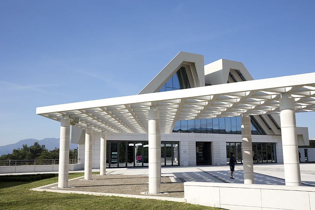 Moderna bijela oproštajna dvorana i natkriveni trg s bijelim stupovima na gradskom groblju pod vedrim nebom.