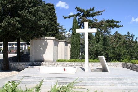 Veliki bijeli kameni križ na uređenom platou groblja Zamet okružen čempresima i borovima.