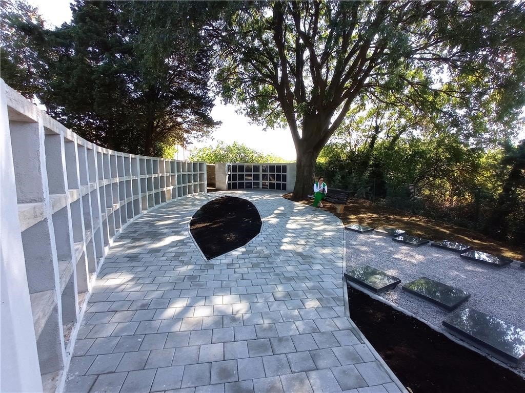 Uređeni prostor za groblje kućnih ljubimaca s polukružnim zidom za urne, popločanom stazom i zelenilom.