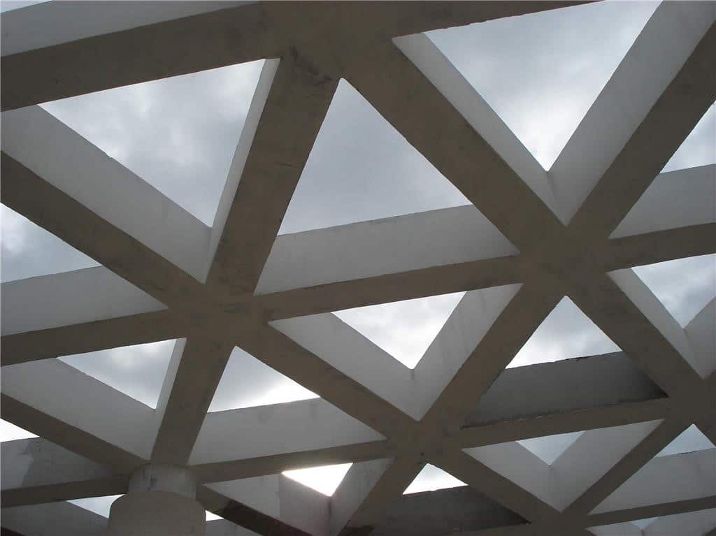 Geometrijska betonska krovna konstrukcija s trokutastim otvorima prema oblačnom nebu na groblju.